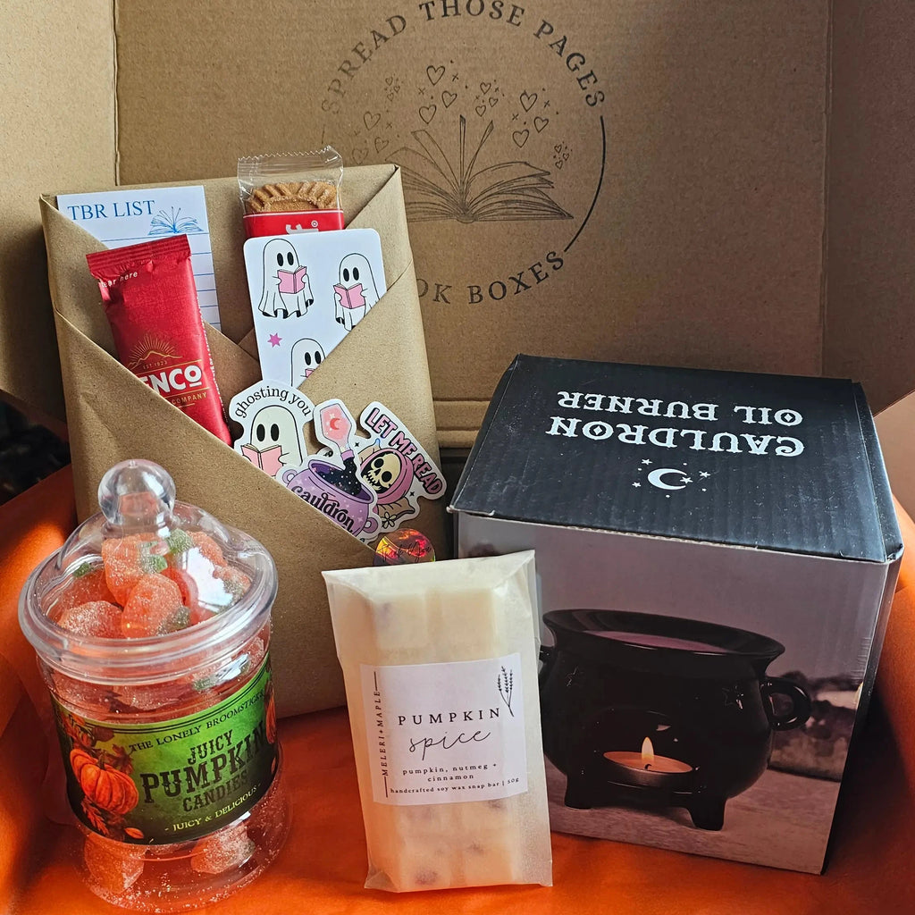 A curated gift box or subscription box from 'SPread Those Pages Book Boxes' containing various items: a jar of orange gummy candies, a pumpkin spice wax melt, a blind date with a book, a black witches cauldron wax burner, all arranged inside a brown cardboard box with an orange interior.