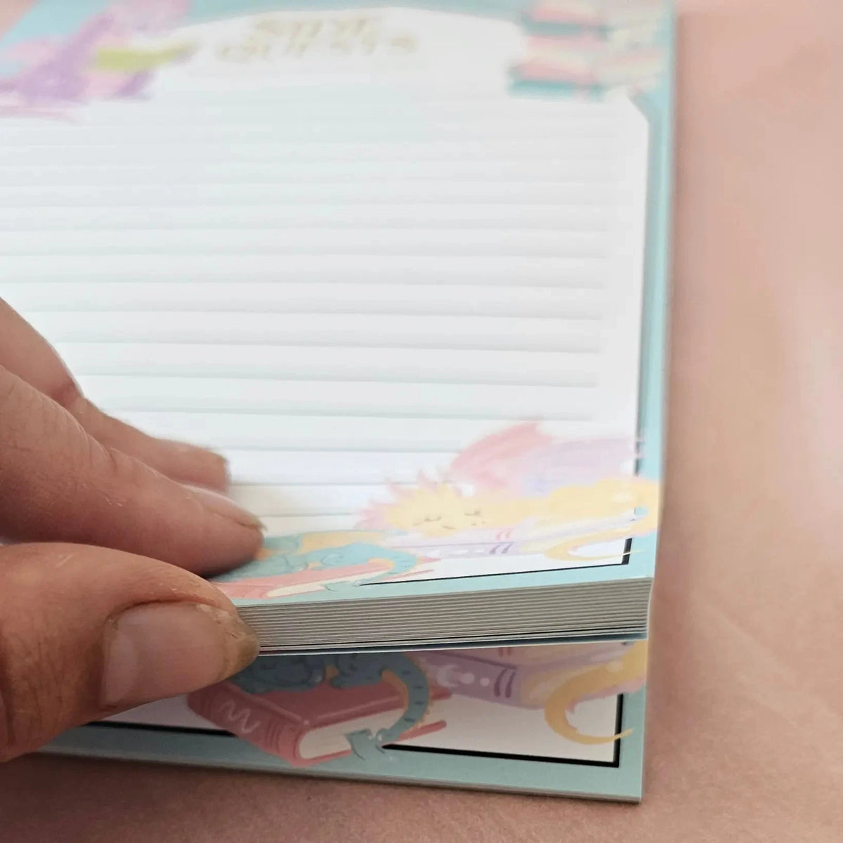 "Close-up of Dragon notepad showing thick lined pages and colourful fantasy illustrations on teal cover"