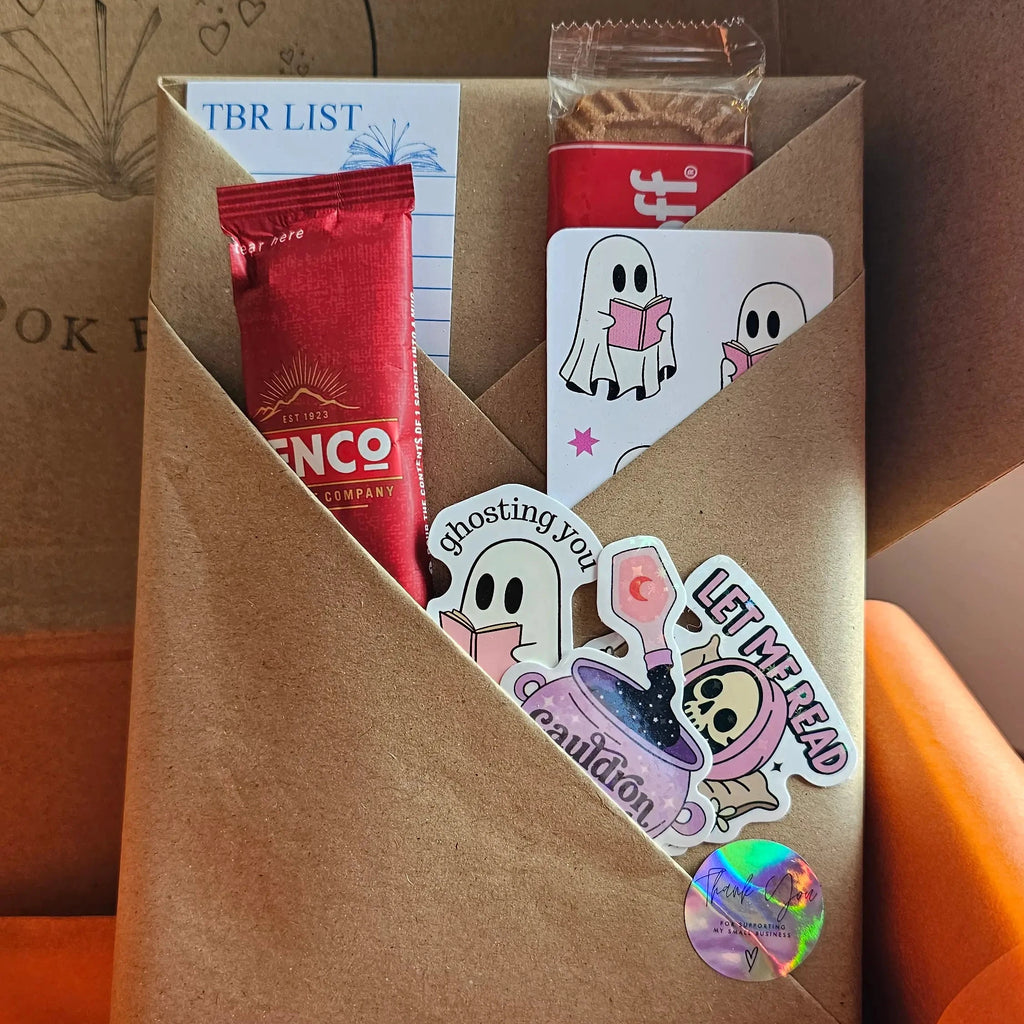"Close-up of Spread Those Pages Halloween book box blind date with a book, with a pumpkin spiced latte sachet, biscoff biscuit, a ghost bookmark, a TBR (To Be Read) card and halloween themed bookish stickers