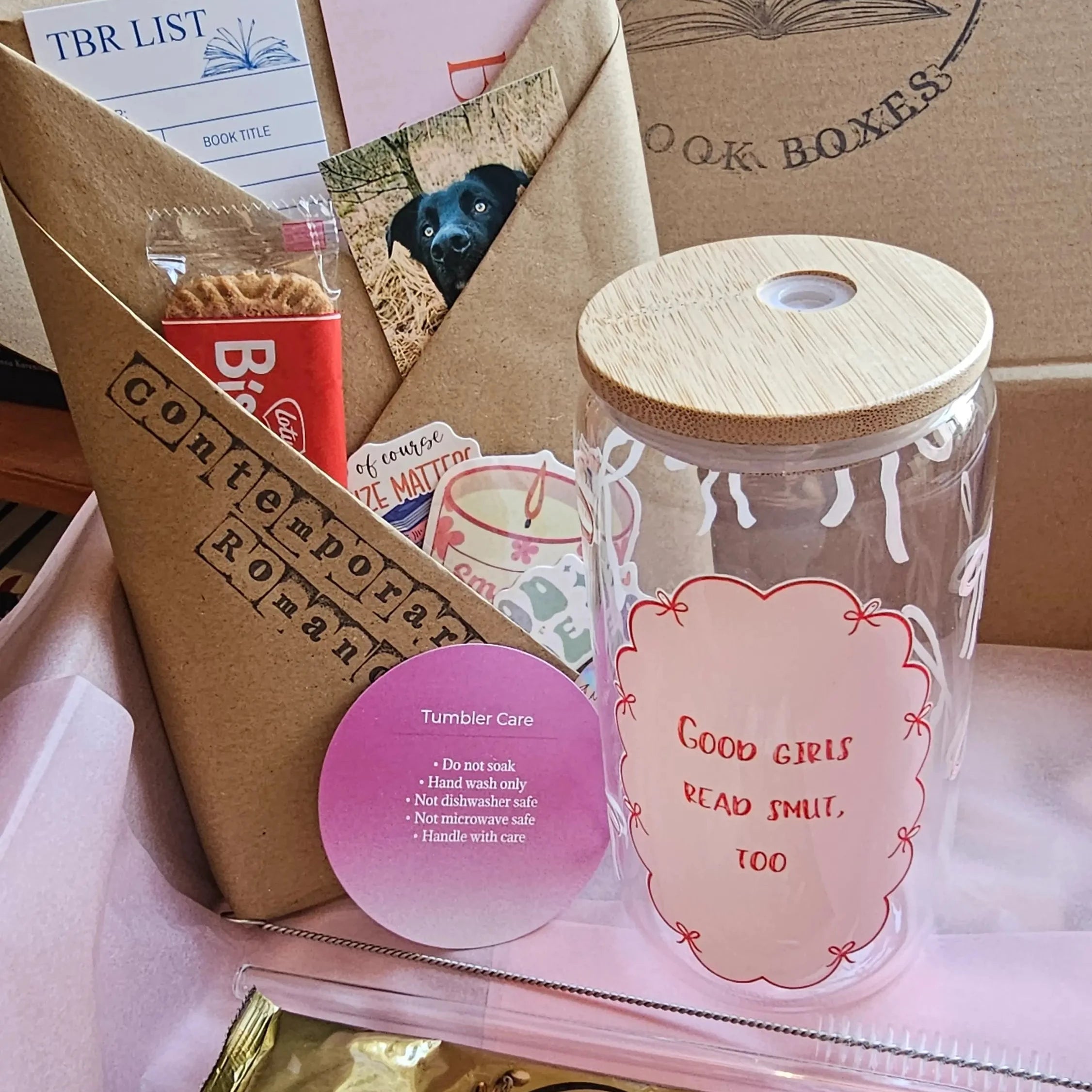 Book and Tumbler Bundle laid out in a Spread Those Pages box, featuring a 16oz glass tumbler with bamboo lid, that reads Good Girls Read Smut, Too, a wrapped Blind Date with a Book in Contemporary Romance, a TBR list notepad, stickers, and matcha latte sachets"