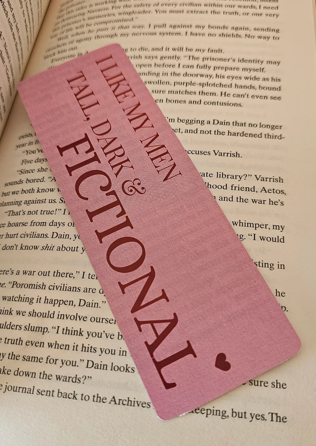 "Pink romance bookmark reading 'I Like My Men Tall, Dark and Fictional' resting on a romantasy book"