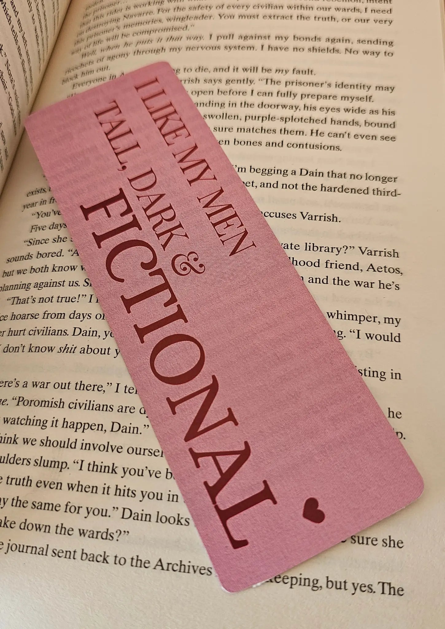 "Pink romance bookmark reading 'I Like My Men Tall, Dark and Fictional' resting on a romantasy book"