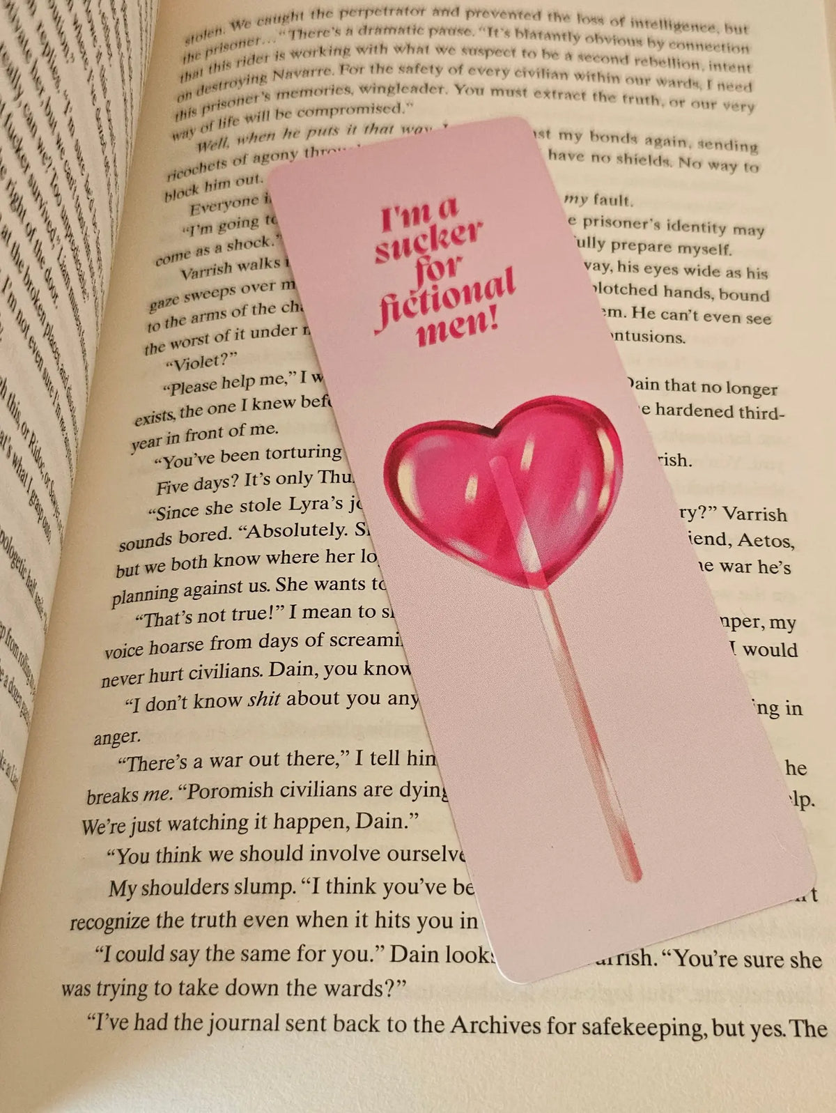  "Pink romance bookmark with lollipop reading 'I'm a Sucker for Fictional Men' on open romantasy book pages"
