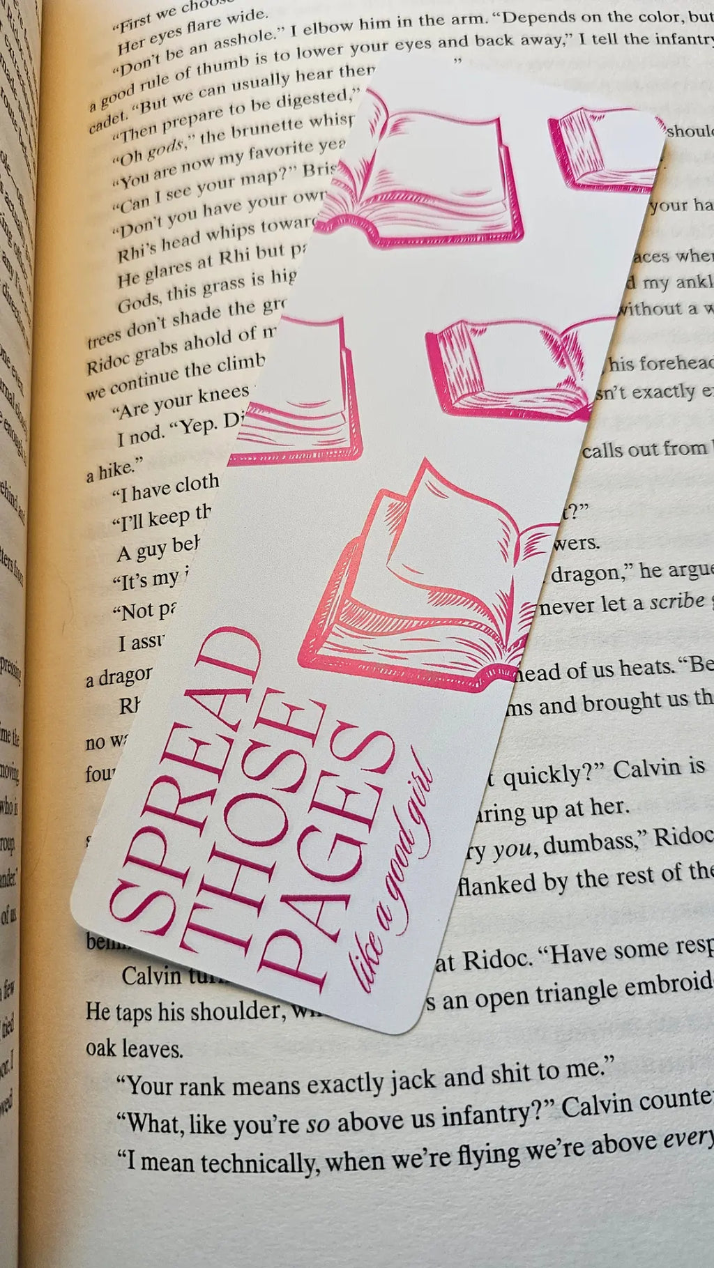 Pink romance bookmark reading 'Spread Those Pages Like a Good Girl' resting on a romantasy book"
